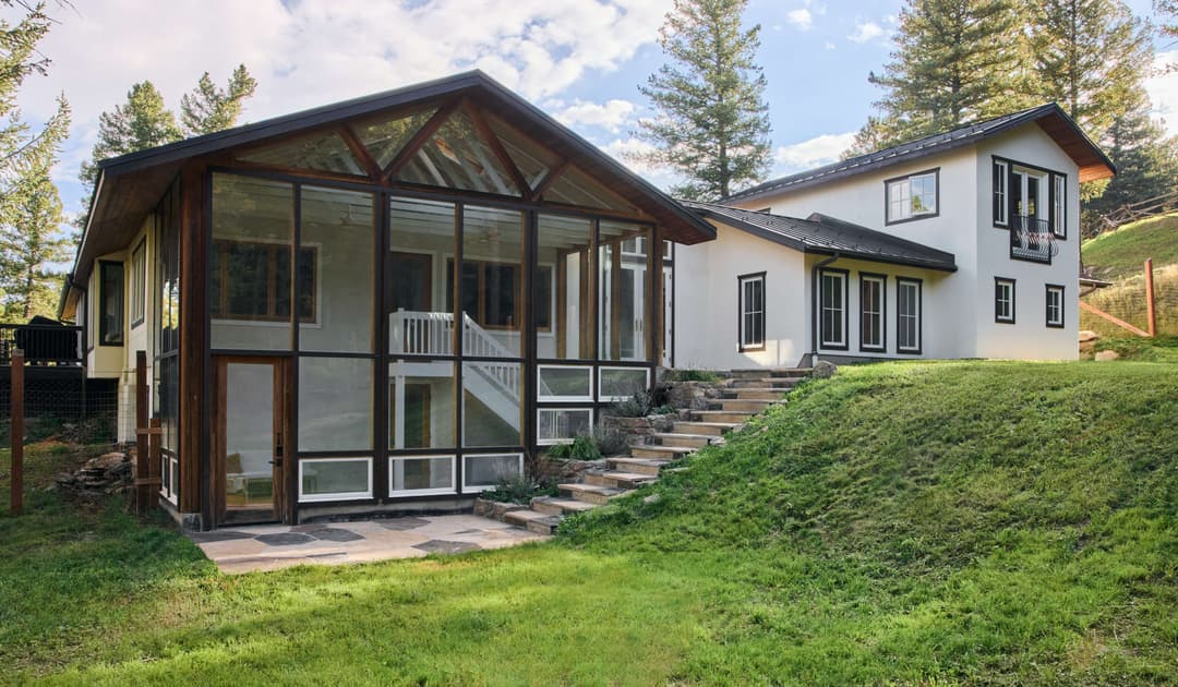 Modern home with a glass-enclosed patio, surrounded by trees and green landscape.