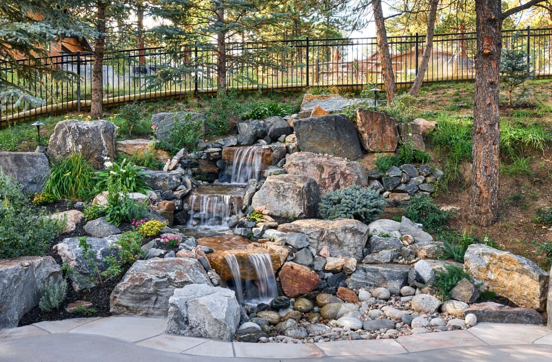 Tranquil garden waterfall surrounded by rocks and greenery in a serene outdoor setting.