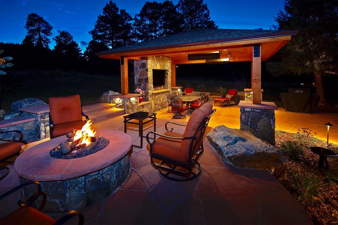 Cozy outdoor living space with a stone fire pit, seating, and ambient lighting at dusk.