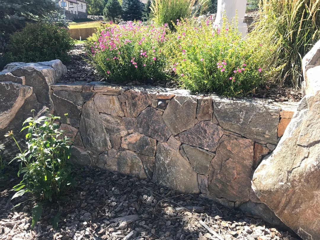 Rock wall garden with flowers and greenery set in a landscaped outdoor area.