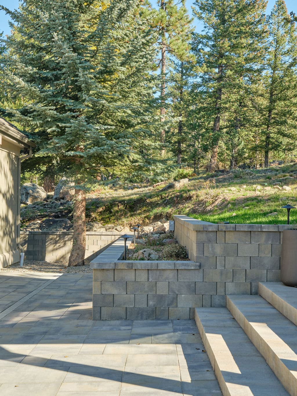 Patio with stone steps and landscaping, nestled in a forested area with tall trees.