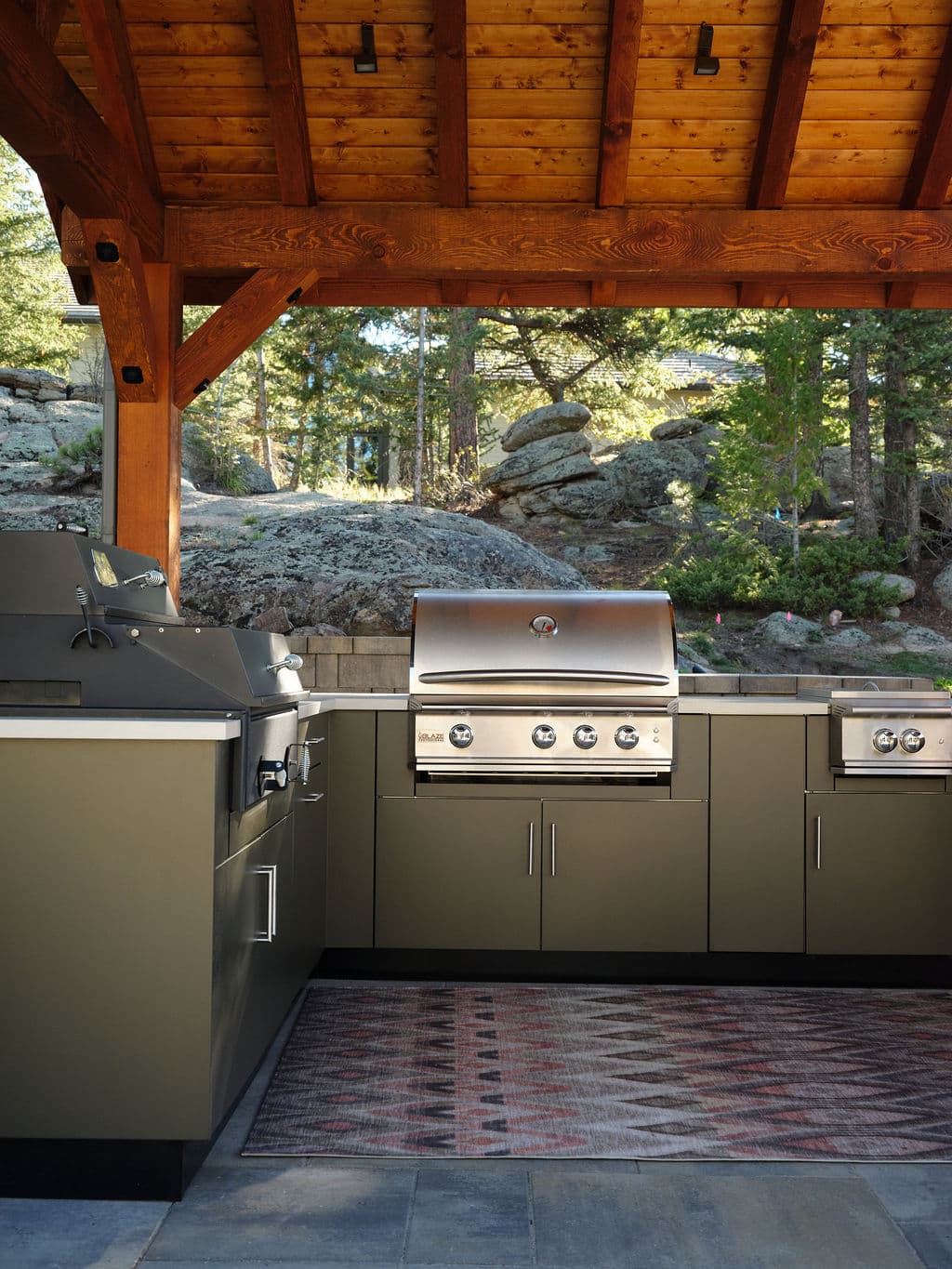Outdoor kitchen with sleek gray cabinets and modern grills under a wooden pavilion.