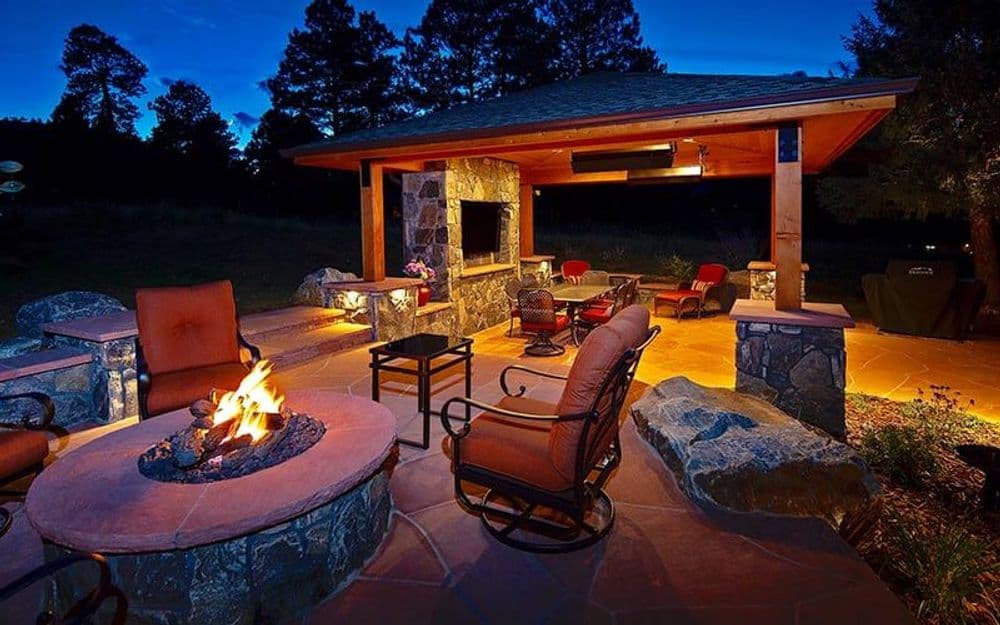 Cozy outdoor patio with stone fireplace, seating area, and ambient evening lighting.