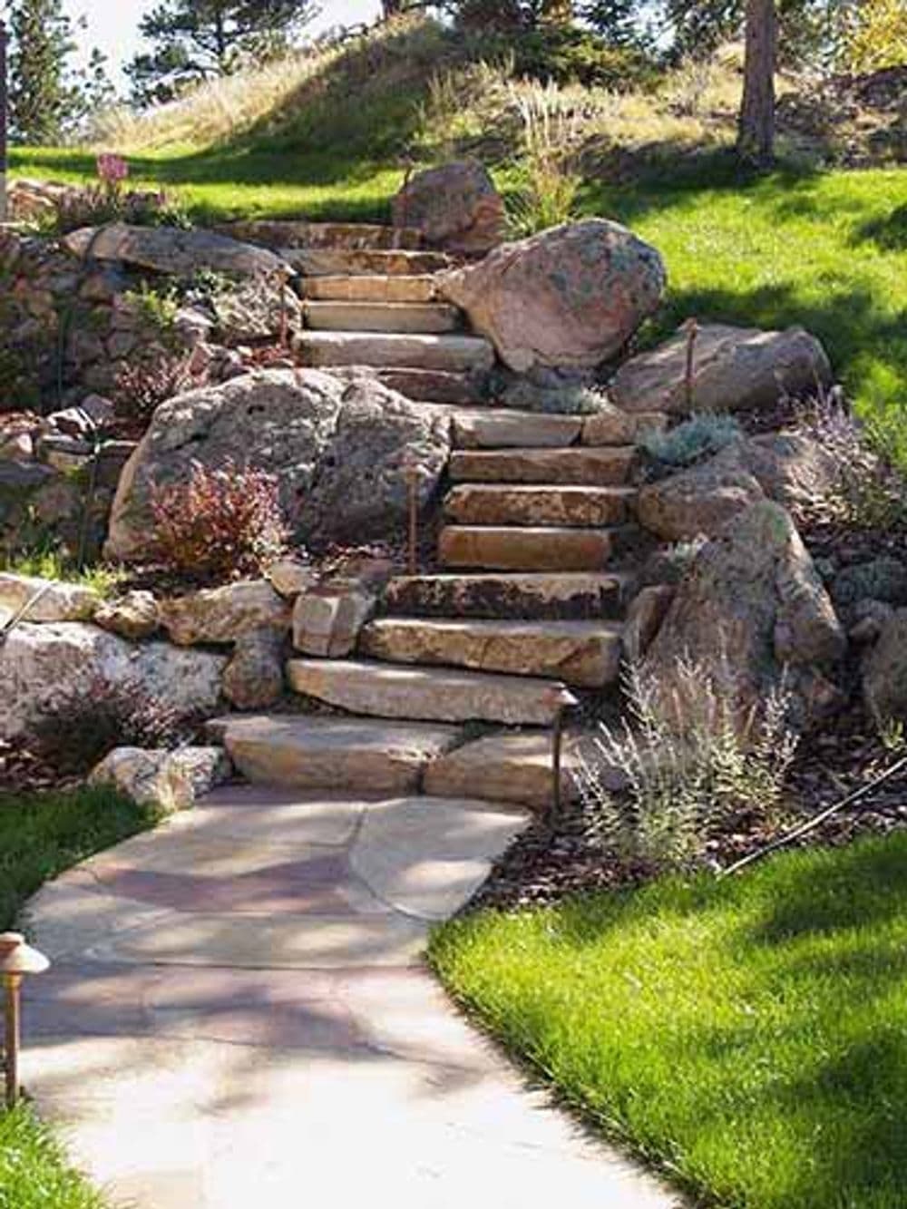 Stone garden steps winding through lush green grass and colorful landscaping rocks.