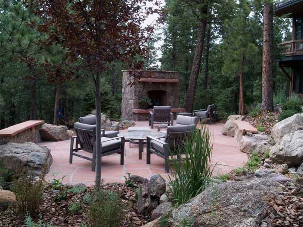 Cozy outdoor seating area with stone fireplace surrounded by trees and natural landscaping.