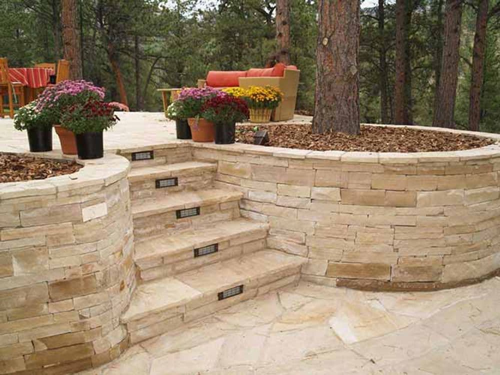 Stone patio with steps, planters of flowers, and trees in a serene outdoor setting.