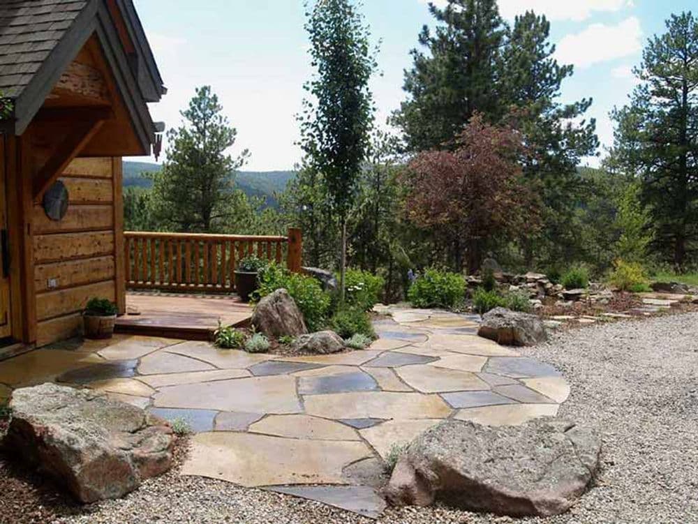 Natural stone patio with wooden deck, surrounded by greenery and scenic mountain views.
