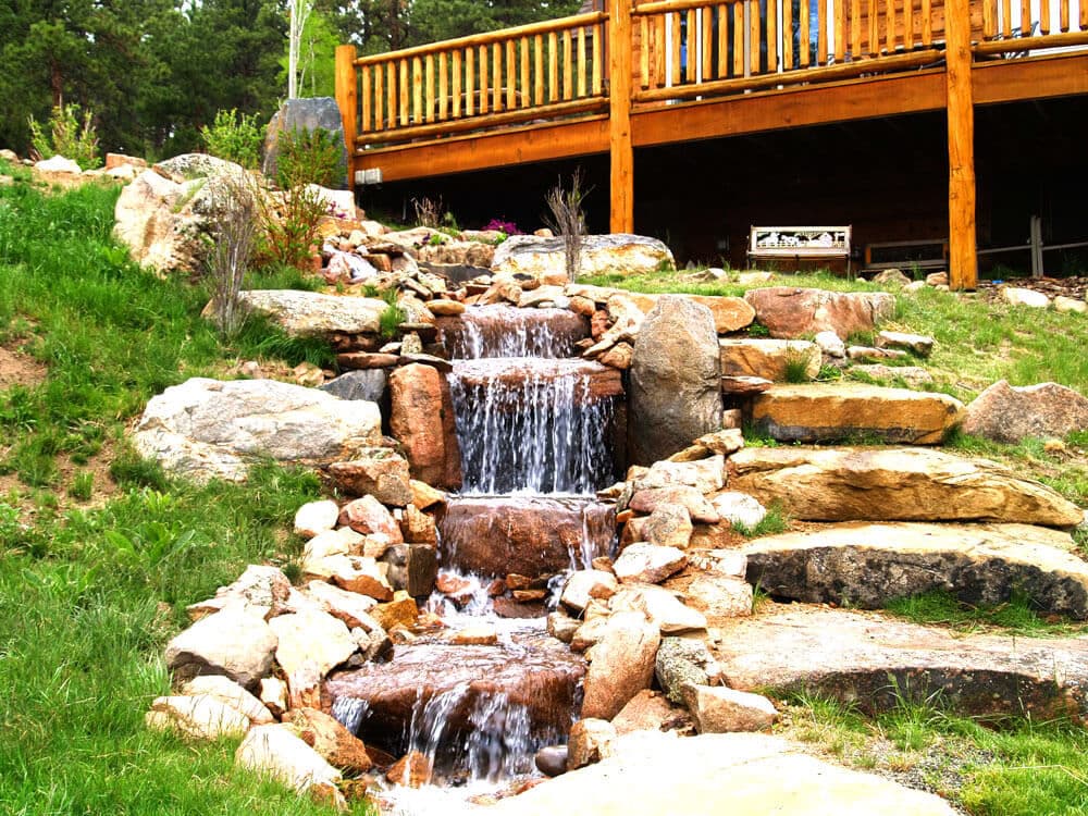Picturesque water feature with cascading stream and rocky landscape, near wooden deck.