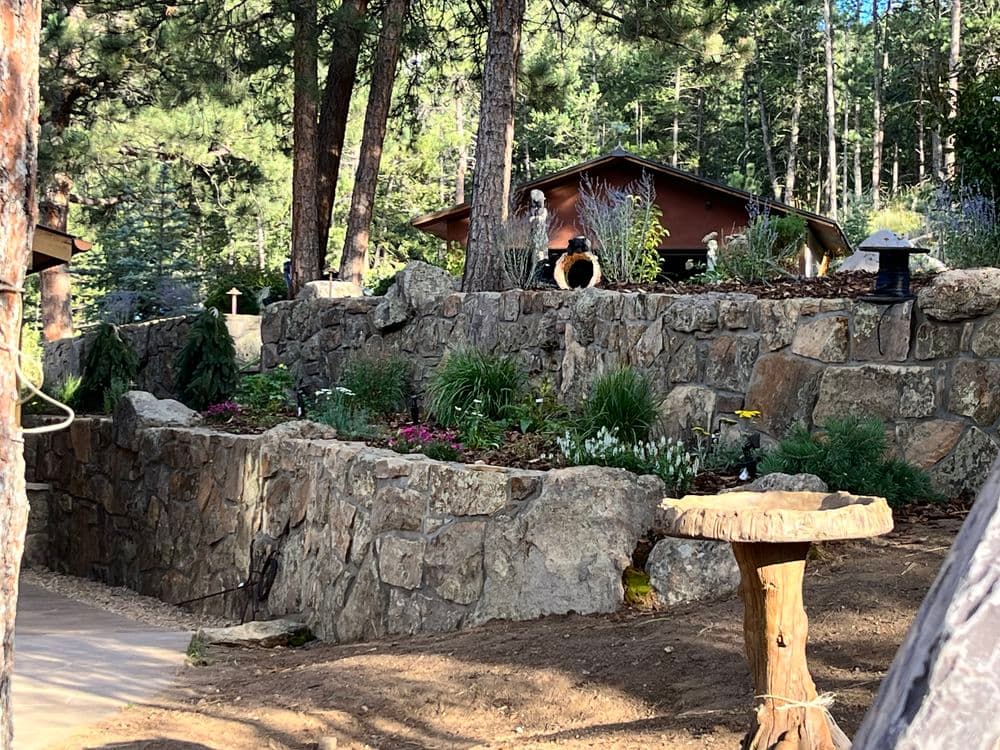 Beautiful stone garden landscape with vibrant flowers and rustic decor in a forest setting.