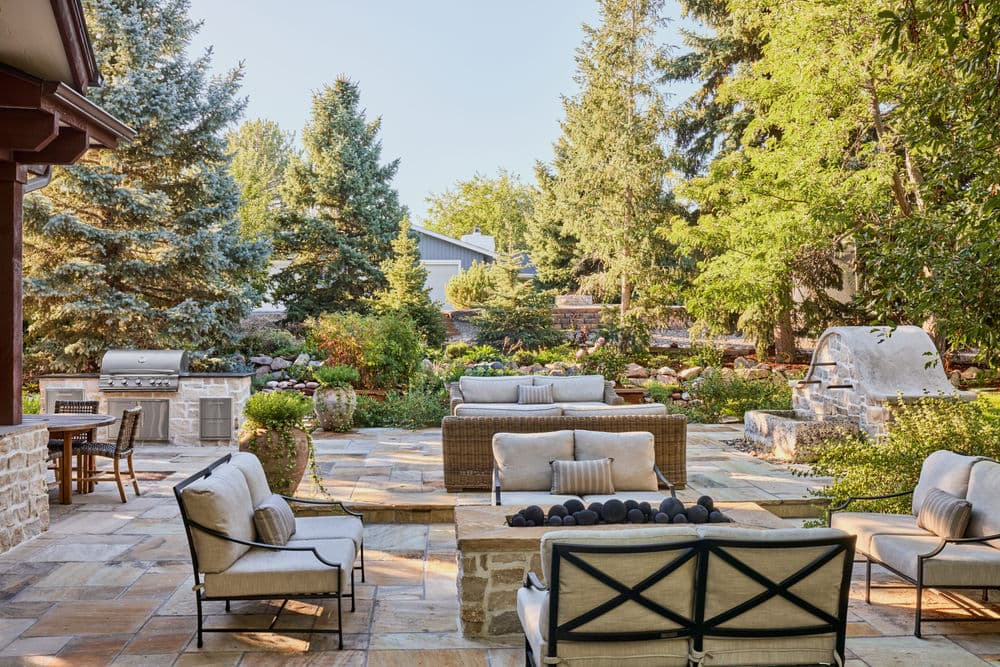 Elegant outdoor living space with comfortable seating, stone patio, and lush greenery.