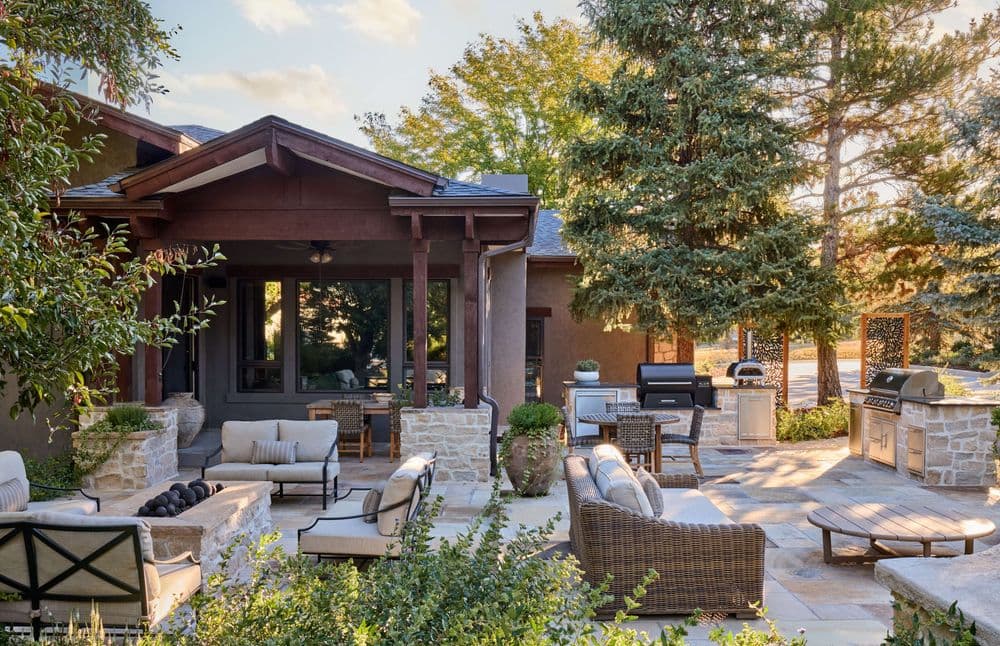 Elegant outdoor patio with seating, grill area, and lush greenery in a serene setting.