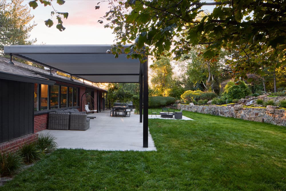 Modern home exterior with patio seating, green lawn, and landscaped garden at sunset.